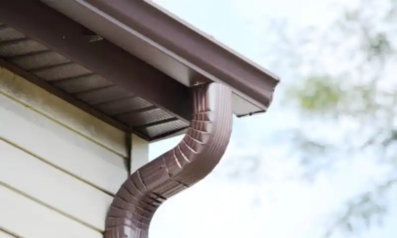 Brown aluminum downspout elbow on a home with light siding