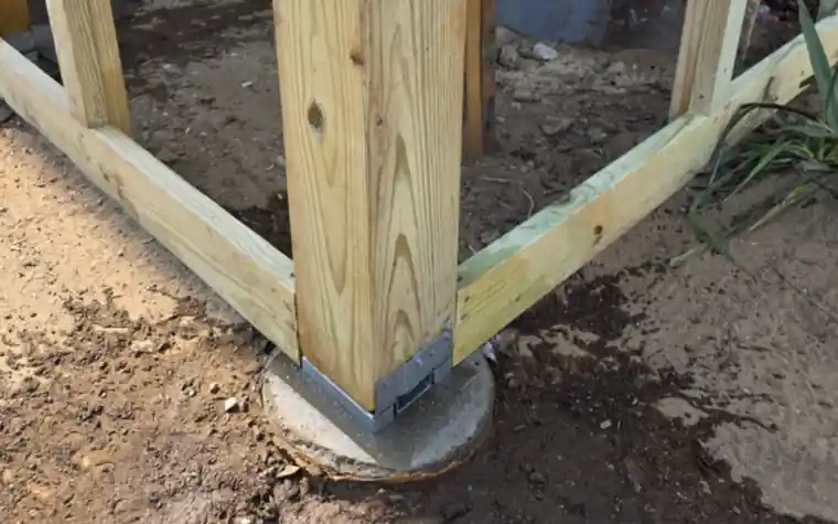 Pressure-treated porch post on a metal post base and concrete footing